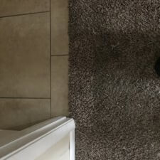 A bathroom with a brown carpet and white tile.